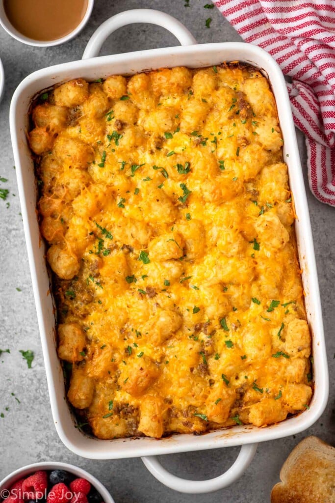 Overhead view of a baking dish of tater tot breakfast casserole with cups of coffee and bowl of berries beside.