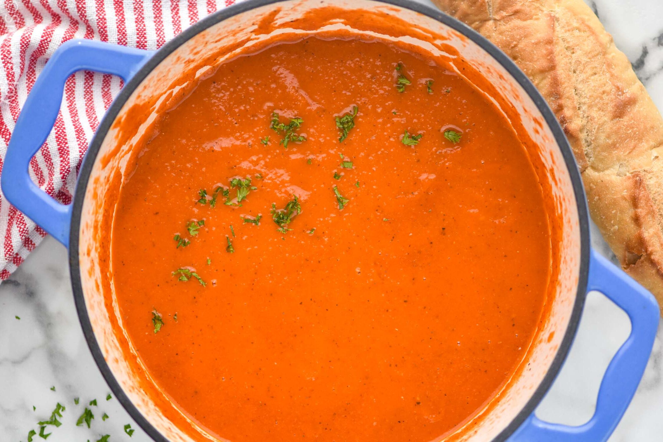 Overhead view of a pot Tomato Soup garnished with parsley. Loaf of bread beside.