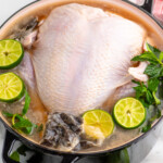 Pot with turkey, sliced limes, mint leaves, tea bags, and seasonings for turkey brine recipe.