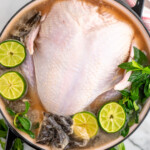 Overhead view of large pot with raw turkey, limes, mint leaves, tea bags, liquid, and spices for turkey brine recipe. - 13