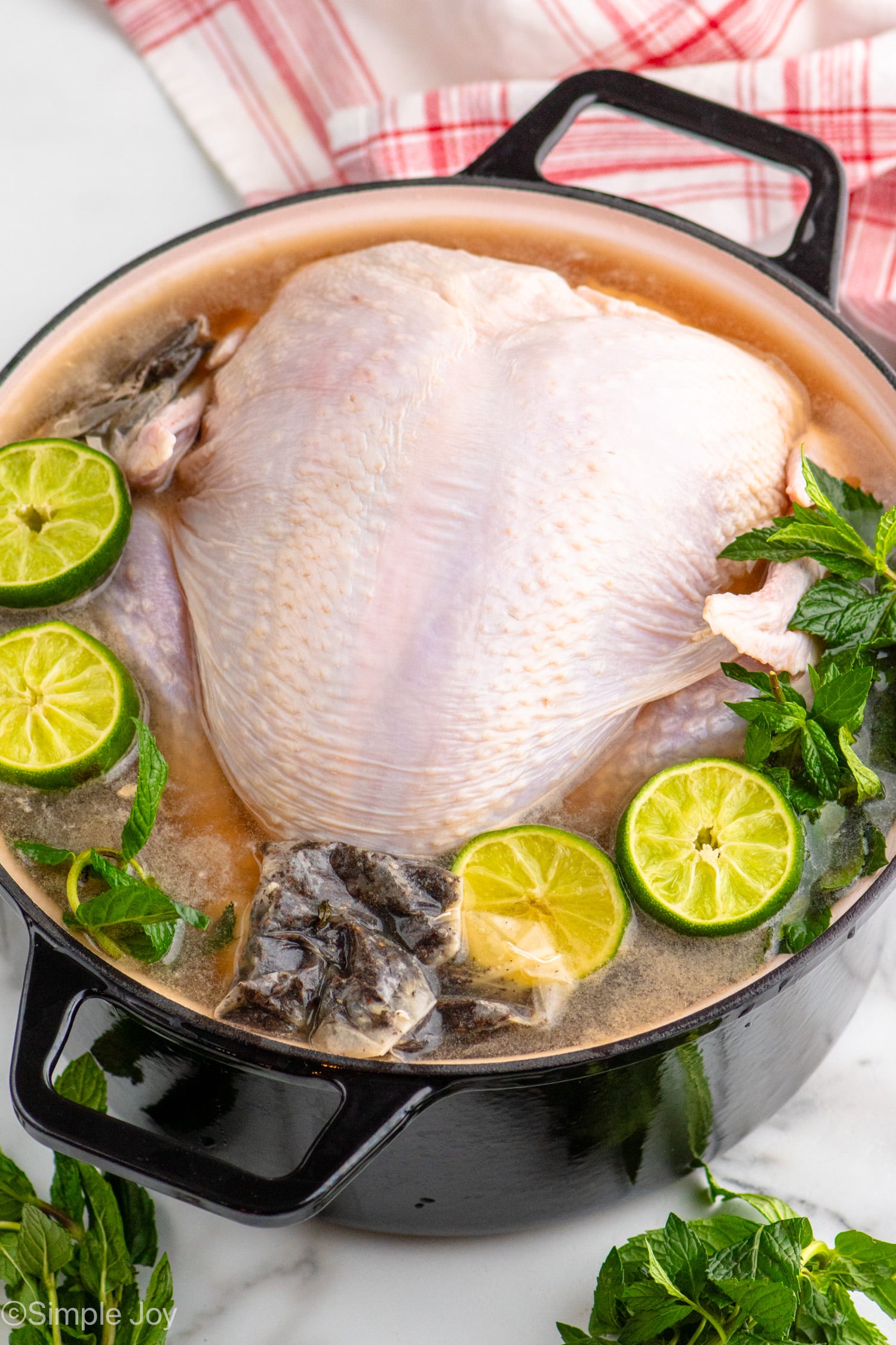 Pot with turkey, sliced limes, mint leaves, tea bags, and seasonings for turkey brine recipe.