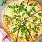 Overhead view of White Pizza sliced and topped with arugula. - 11