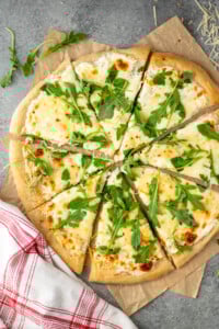Overhead view of White Pizza sliced and topped with arugula. - 10