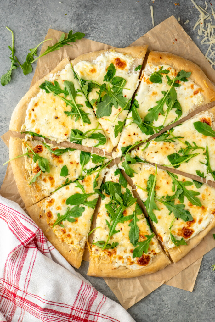 Overhead view of White Pizza sliced and topped with arugula. - 2