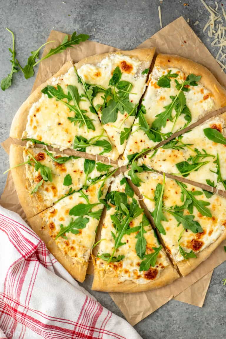 Overhead view of White Pizza sliced and topped with arugula.