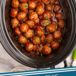 Pinterest graphic for Grape Jelly Meatballs recipe. Image shows overhead view of a crockpot of Grape Jelly Meatballs garnished with parsley. Text says, "3 ingredient Grape Jelly Meatballs simplejoy.com."