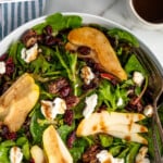 Pinterest graphic for Pear Salad recipe. Text says, "the best Pear Salad recipe simplejoy.com." Image shows overhead view of a bowl of Pear Salad with forks, dressing, glass of white wine, and bread beside.