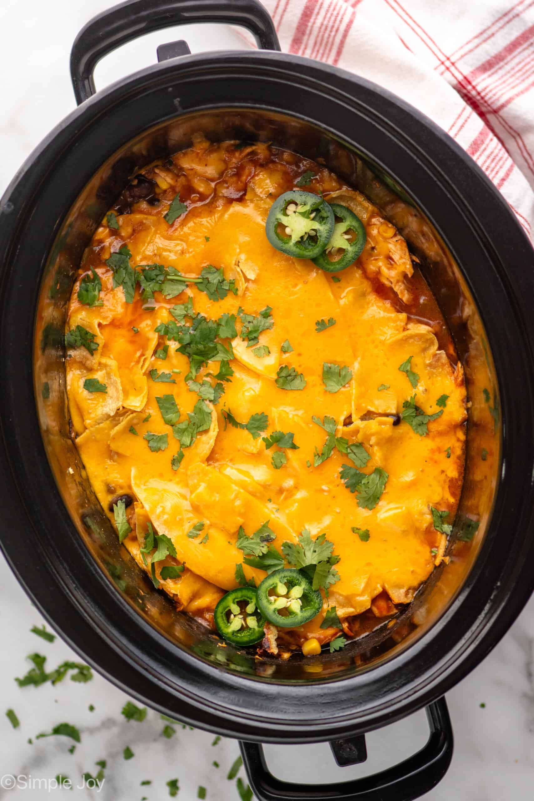 Overhead view of a crockpot of Crockpot Chicken Enchilada Casserole recipe, topped with cilantro and jalapenos