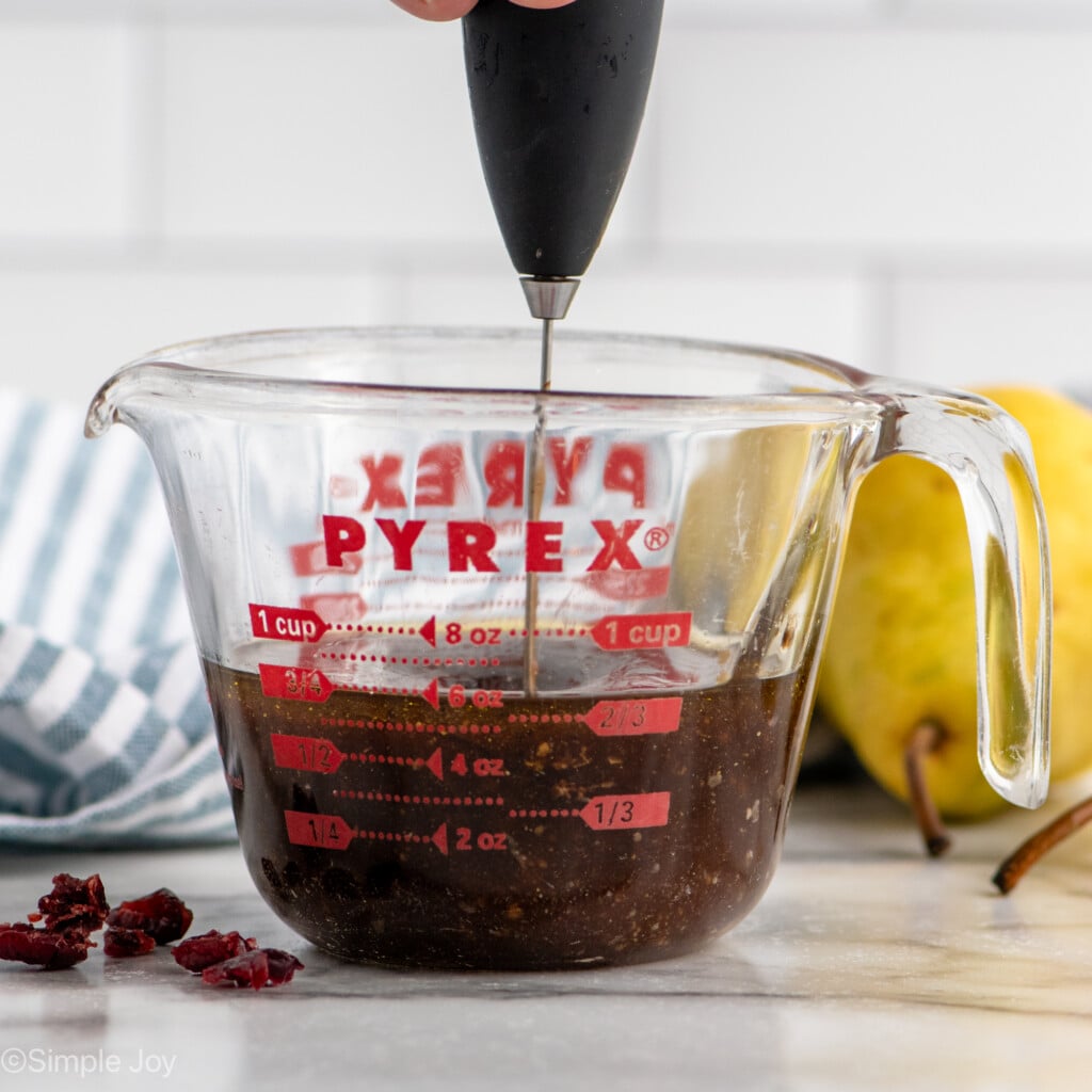 Side view of glass measuring cup of Pear Salad dressing with immersion blender mixing it together.