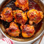 Overhead view of a skillet of Honey Garlic Chicken Thighs with chopped green onions and sesame seeds as garnish.