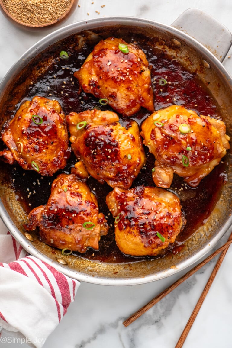 Overhead view of a skillet of Honey Garlic Chicken Thighs with chopped green onions and sesame seeds as garnish.