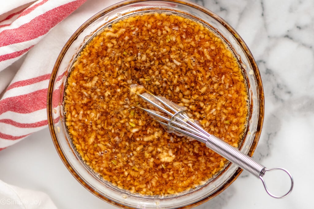 Overhead view of a glass mixing bowl of ingredients with whisk for Honey Garlic Chicken Thighs recipe.