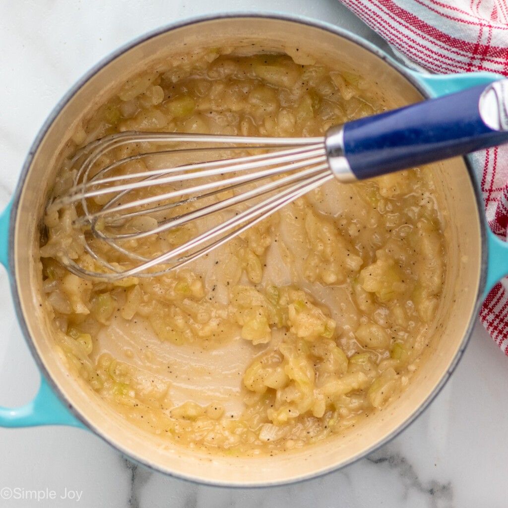 Overhead view of a pot of ingredients with a whisk for Potatoes Au Gratin recipe.