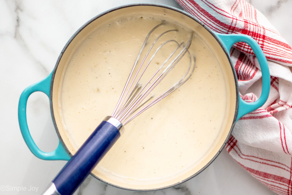Overhead view of a pot of sauce ingredients and whisk for Potatoes Au Gratin recipe