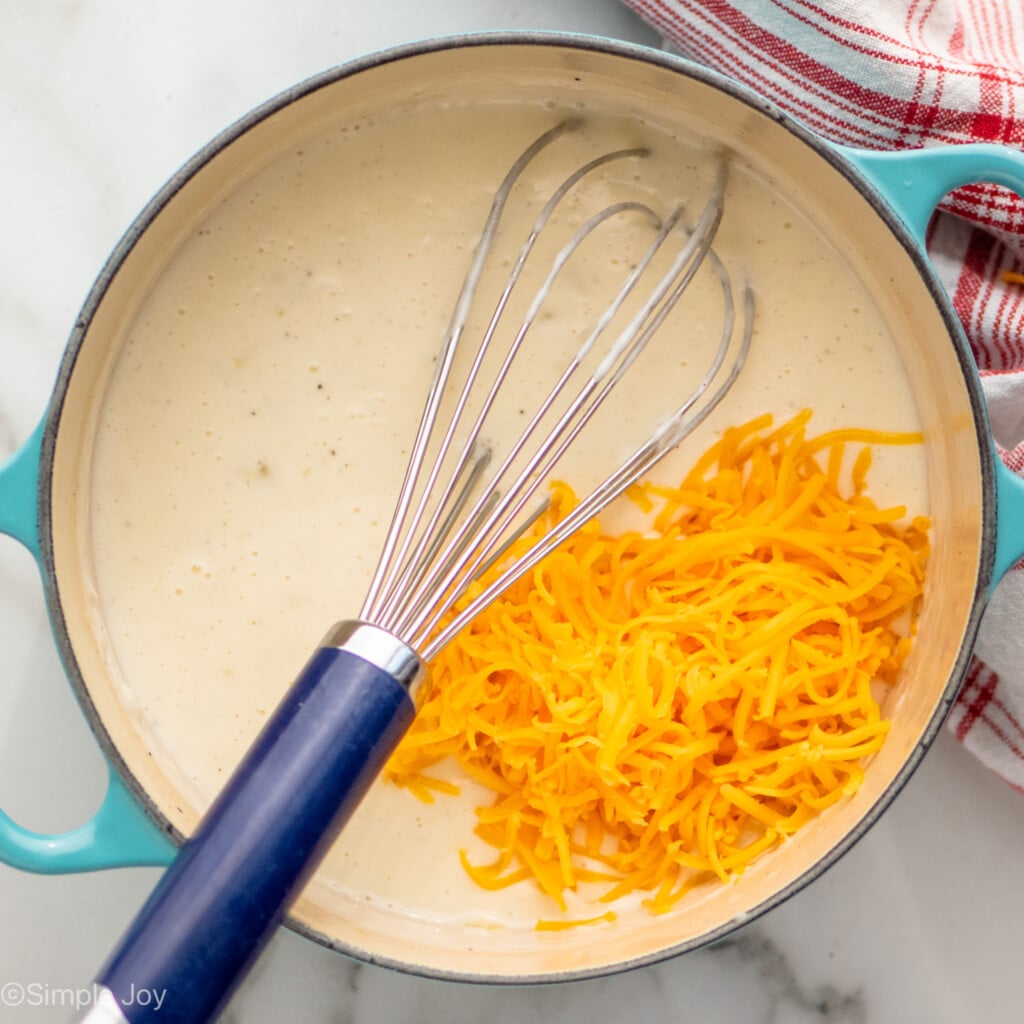 Overhead view of a pot of ingredients for Potatoes Au Gratin recipe with whisk for stirring. - 7