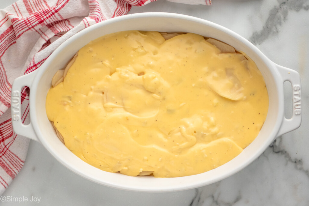 Overhead view of a baking dish of Potatoes Au Gratin recipe with sauce on top before baking