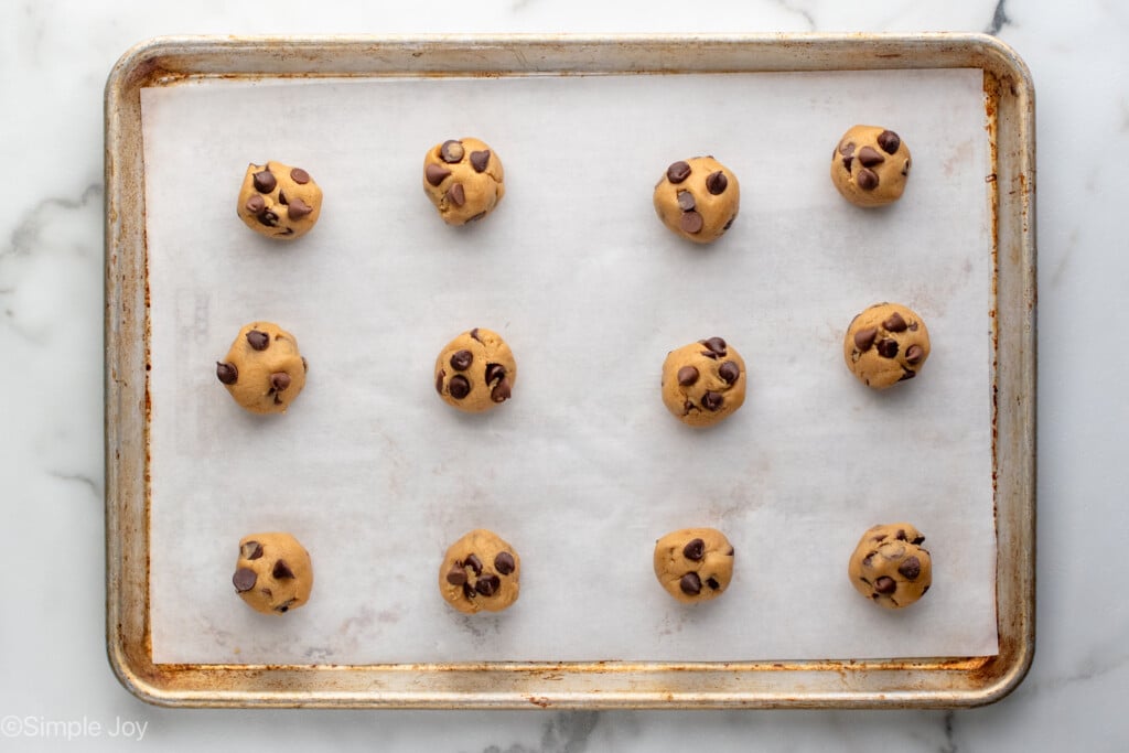 Overhead view of baking sheet with parchment paper and balls of Brown Butter Chocolate Chip Cookies dough before baking. - 11