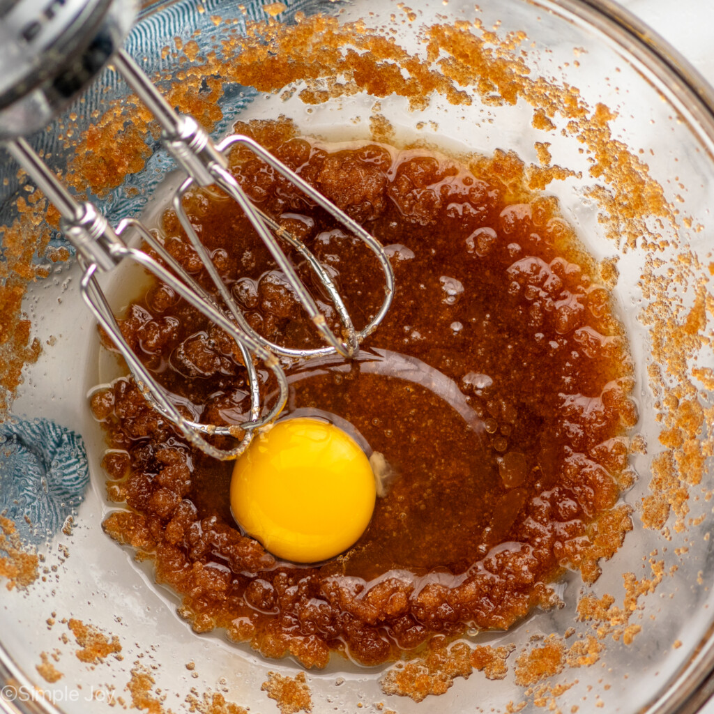 Overhead view of a glass mixing bowl of wet ingredients and hand mixer for Brown Butter Chocolate Chip Cookies recipe