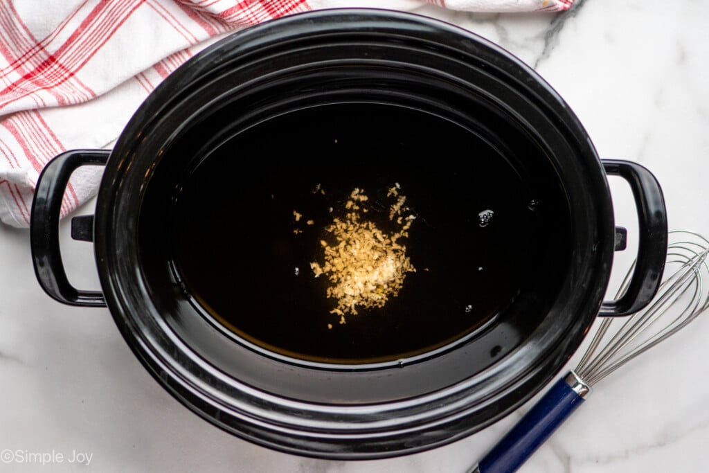 Overhead view of a crockpot with garlic, whisk beside, for Crock Pot Chicken Marsala recipe - 6