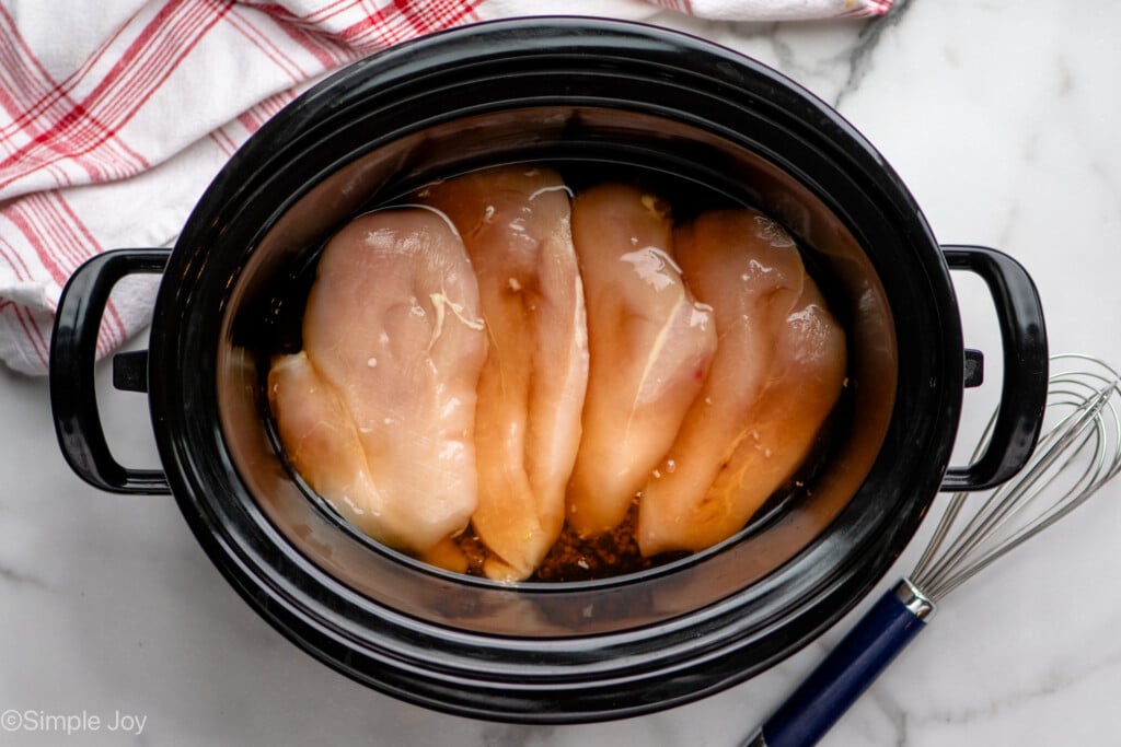 Overhead view of crockpot with raw chicken breasts in liquid for Crock Pot Chicken Marsala, whisk beside. - 7