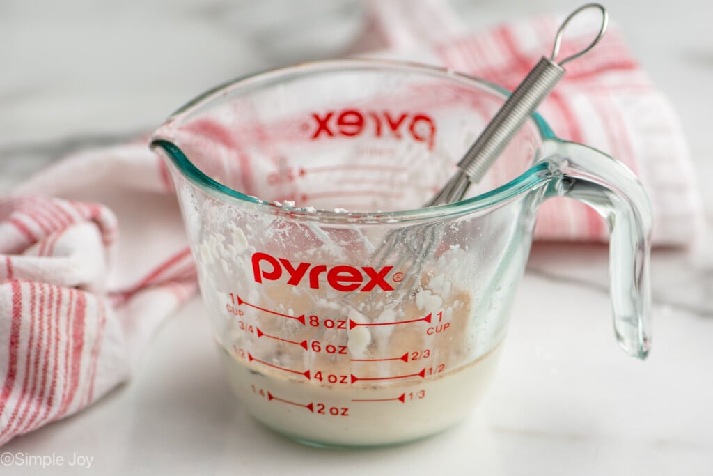 Side view of a glass measuring cup with slurry and whisk for Crock Pot Chicken Marsala recipe - 9