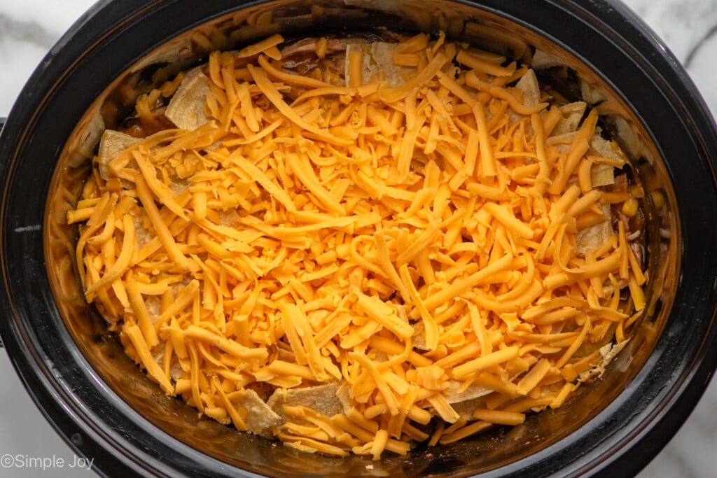 Overhead view of crock pot with Crockpot Chicken Enchilada Casserole recipe, topped with shredded cheese before cooking. - 7