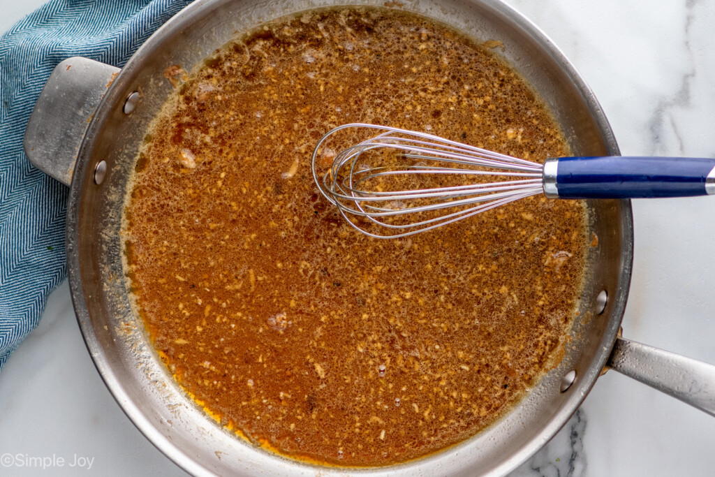 Overhead view of a skillet of ingredients for Honey Garlic Chicken Thighs recipe with a whisk