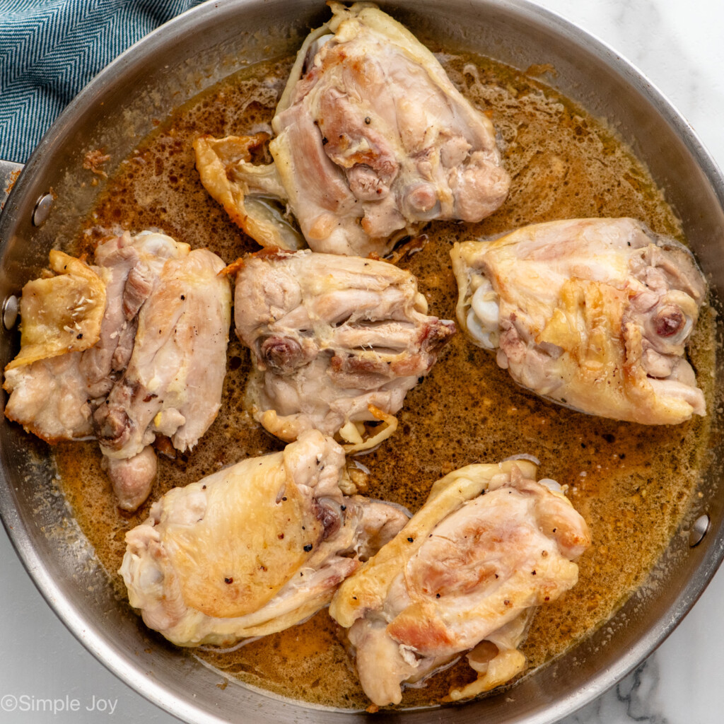 Overhead view of a skillet of raw chicken thighs cooking for for Honey Garlic Chicken Thighs recipe