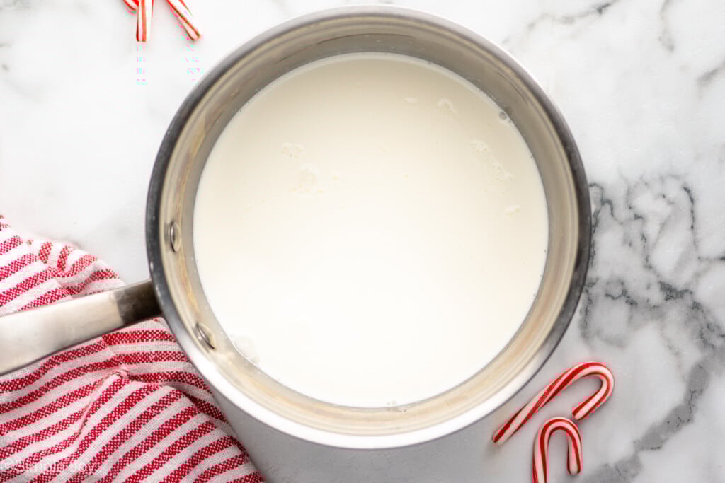 Overhead view of saucepan of ingredients for Peppermint Hot Chocolate recipe, candy canes beside - 3