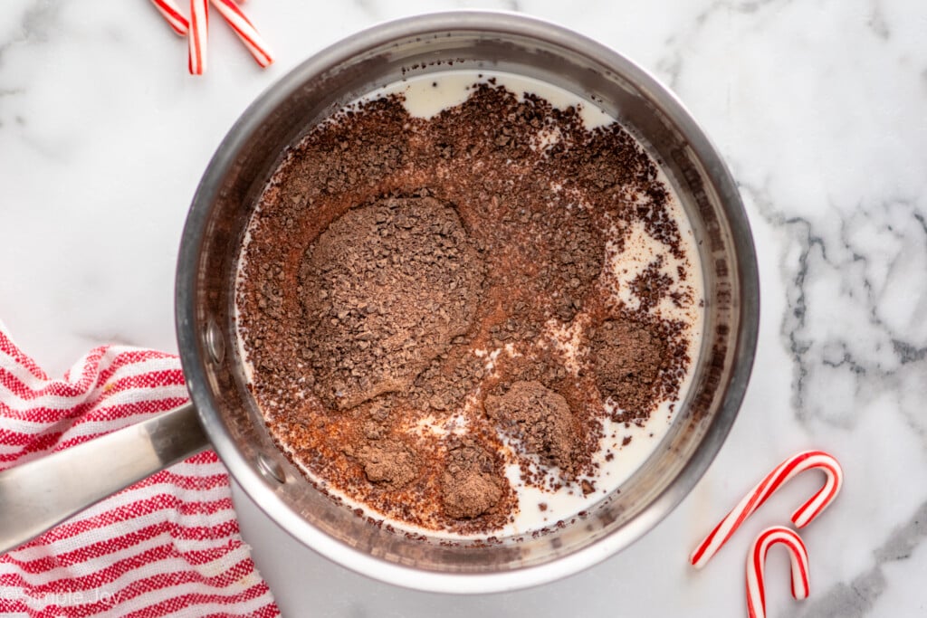 Overhead view of a saucepan of ingredients for Peppermint Hot Chocolate recipe with candy canes beside - 4