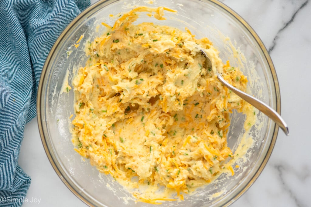 Overhead view of a mixing bowl of Mashed Potato Pancakes recipe ingredients with spoon for mixing. - 6
