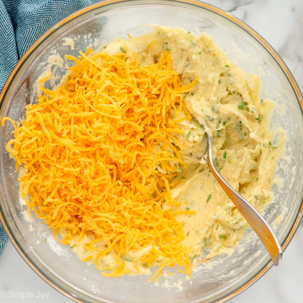 Overhead view of a mixing bowl of ingredients and shredded cheese for Mashed Potato Pancakes recipe with spoon for mixing