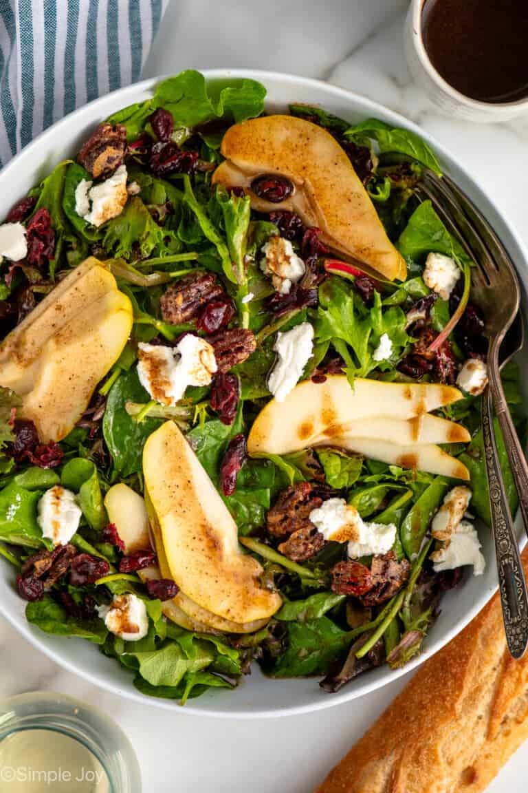 Overhead view of bowl of Pear Salad with forks, glass of white wine and loaf of bread beside