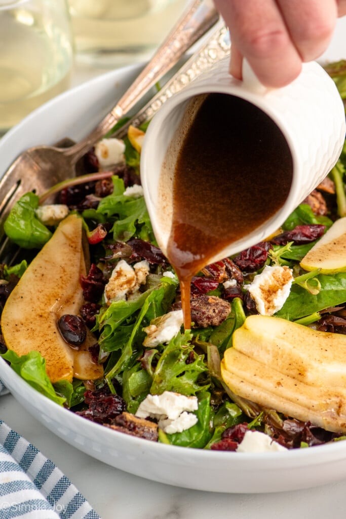 Person's hand pouring dressing over bowl of Pear Salad recipe with forks. - 6