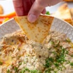 Pinterest graphic for Baba Ganoush recipe. Text says, "the best Baba Ganoush simplejoy.com." Photo shows person's hand scooping Baba Ganoush from bowl, garnished with parsley.