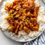 Pinterest graphic for Bourbon Chicken recipe. Image shows overhead view of a plate of rice with Bourbon Chicken garnished with sesame seeds and chopped green onions, chopsticks beside. Text says, "super easy Bourbon Chicken simplejoy.com."