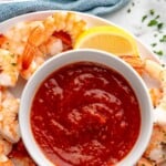 Pinterest graphic for Shrimp Cocktail Sauce recipe. Text says, "homemade cocktail sauce simplejoy.com." Overhead view of a platter of shrimp with a lemon wedge, bowl of Shrimp Cocktail Sauce.