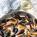 Pinterest graphic for Mussels recipe. Text says, "the best Mussels recipe simplejoy.com." Image shows skillet of Mussels recipe with glass of white wine beside.