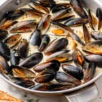 Pinterest graphic for Mussels recipe. Image shows skillet of Mussels with glass of white wine beside. Text says, "super easy Mussels recipe simplejoy.com."