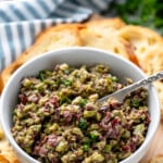 Pinterest graphic for Olive Tapenade recipe. Text says, "the best Olive Tapenade simplejoy.com." Image shows bowl of Olive Tapenade with a knife for spreading surrounded by toasted bread slices.