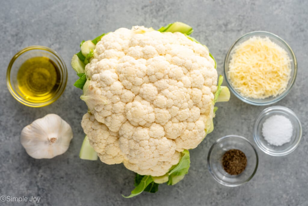overhead of ingredients for air fryer cauliflower: oil, garlic, a head of cauliflower, some shredded parmesan, salt and pepper - 6