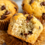 Close up view of banana chocolate chip muffins with a bite taken out of one muffin that is unwrapped. - 15