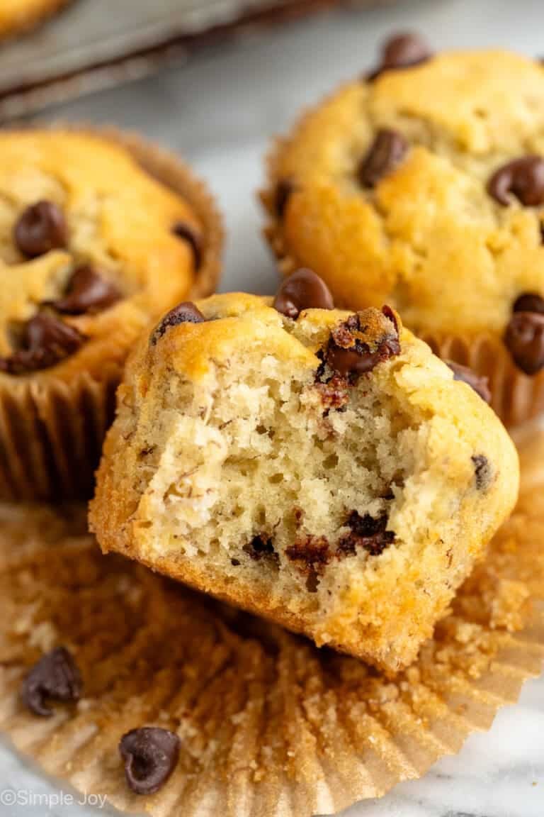 Close up view of banana chocolate chip muffins with a bite taken out of one muffin that is unwrapped.