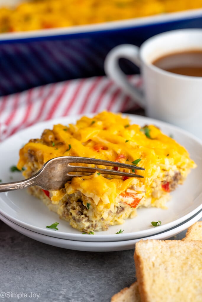 Piece of Hashbrown Breakfast Casserole on a plate with a fork cutting into it, cup of coffee beside