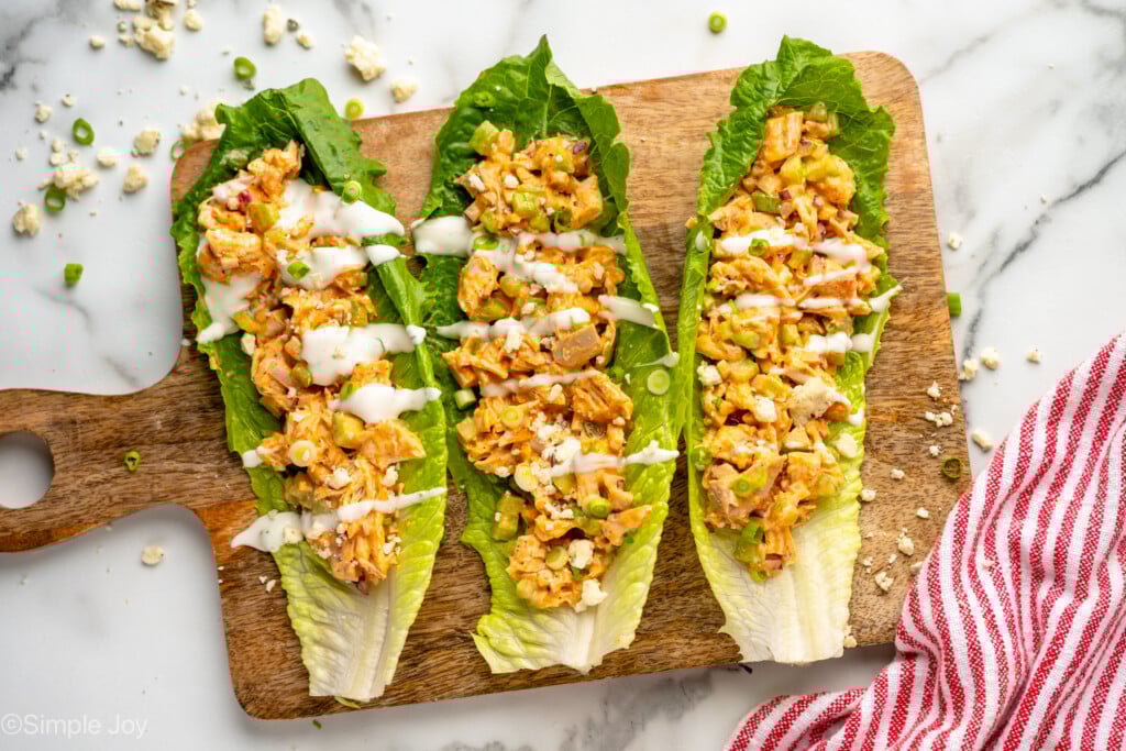 Overhead view of a wooden cutting board with lettuce topped with Buffalo Chicken Salad, garnished with dressing - 6