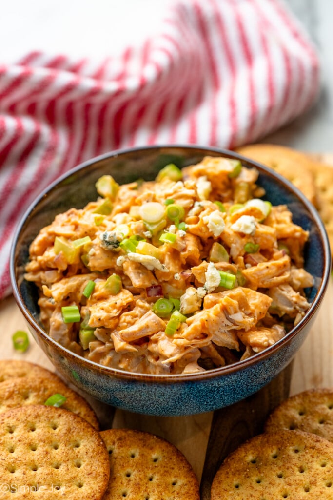Bowl of Buffalo Chicken Salad topped with chopped green onions and blue cheese crumbles, crackers beside. - 10