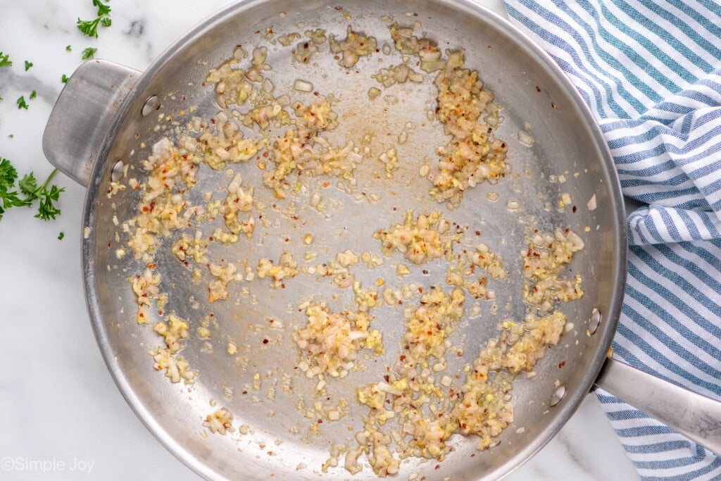 Overhead view of a skillet of garlic and seasonings cooking for Mussels recipe. - 6