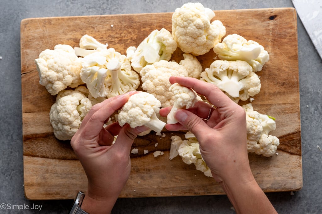 Overhead view of person's hand holding pieces of cauliflower over cutting board of cut up cauliflower - 5