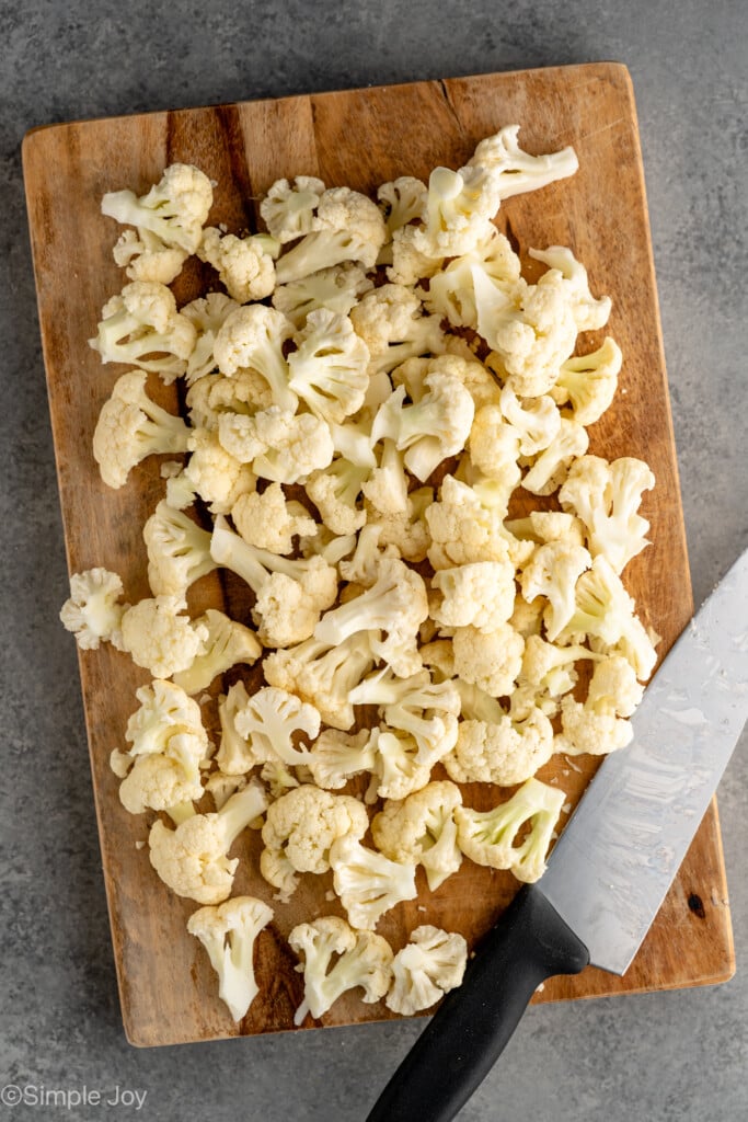 Overhead view of cutting board with cut up cauliflower and a knife for how to cut cauliflower recipe - 1
