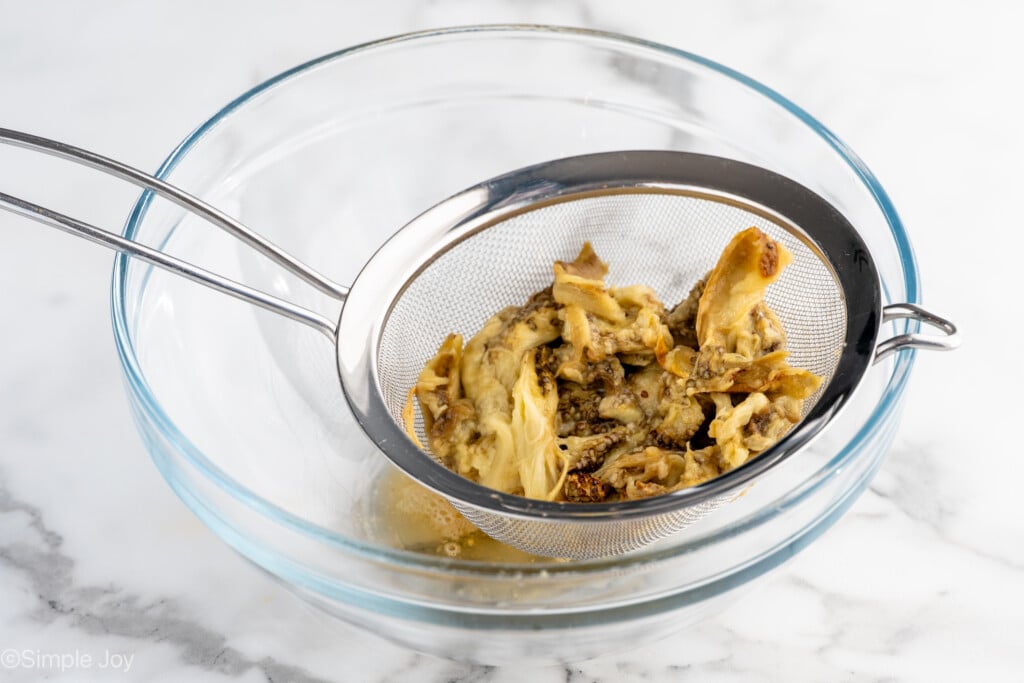 Mixing bowl with a metal sieve of baked eggplant for Baba Ganoush recipe